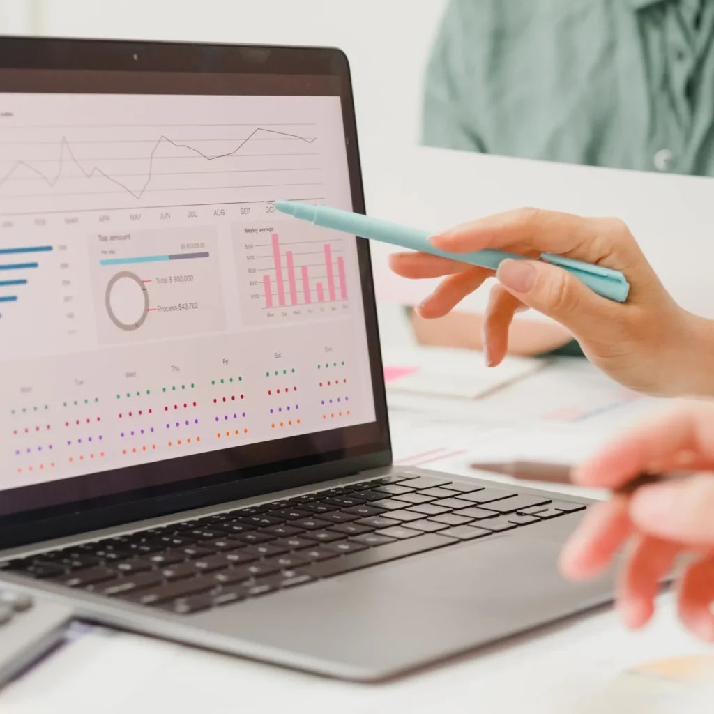 Two people analyze graphs and charts on a laptop screen.